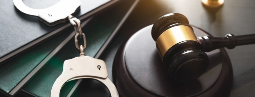 Photo of a judge's gavel and handcuffs on top of books.