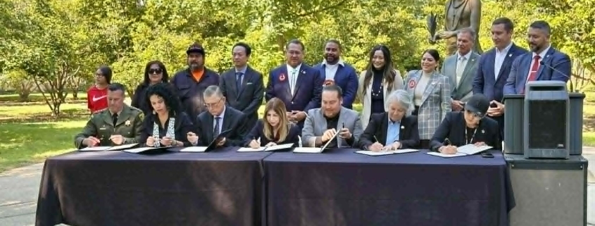 Foto de Presidentes Tribales, Fiscal de Distrito y Sheriff Anunciando Colaboración sobre Personas Indígenas Desaparecidas y Asesinadas; todos estan sentados en una Firmando MOU en un parque frente a una estatua indígena en Sacramento