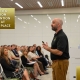Photo of man talking in front of audience in a big room with a screen behind him.