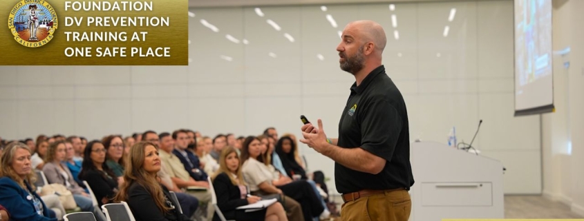 Photo of man talking in front of audience in a big room with a screen behind him.