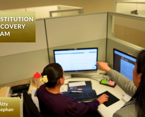 Two members of the San Diego District Attorney's Restitution Recovery Team working together at a desk, reviewing information on computer monitors in an office cubicle.