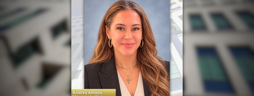 Retrato profesional de Andrea Amado con un saco oscuro y una blusa blanca con cuello en V, usando un collar y aretes de aro, frente a un fondo azul de estudio, con un texto que dice “Andrea Amado, Investigadora III de la Fiscalía de Distrito” y “Mes de la Herencia Hispana.”