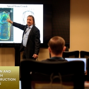 A man stands in front of a screen projector showing the image of a car to an audience in a classroom training room.