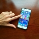 A woman's finger is clicking through the apps on the screen of an Apple iPhone cell phone resting on a desk.